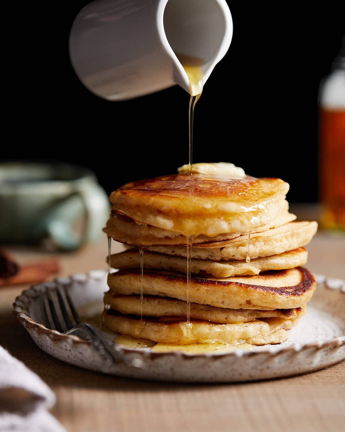 Side profile of homemade pancakes with syrup being poured over them.