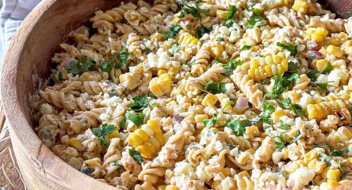 Up close image of elote pasta salad with garnish in wooden bowl.