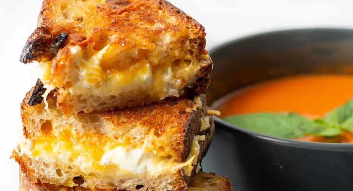 Up close image of grilled cheese sandwich with bowl of tomato soup next to it.