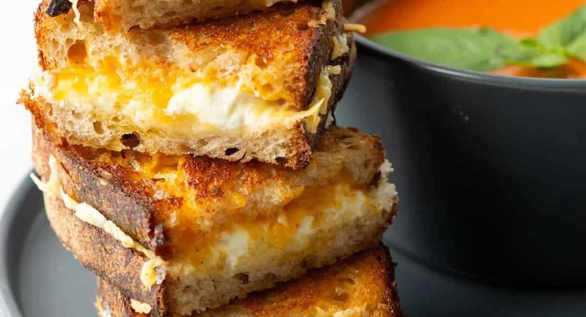 Side profile image of four cheese grilled cheese with bowl of tomato soup next to it.
