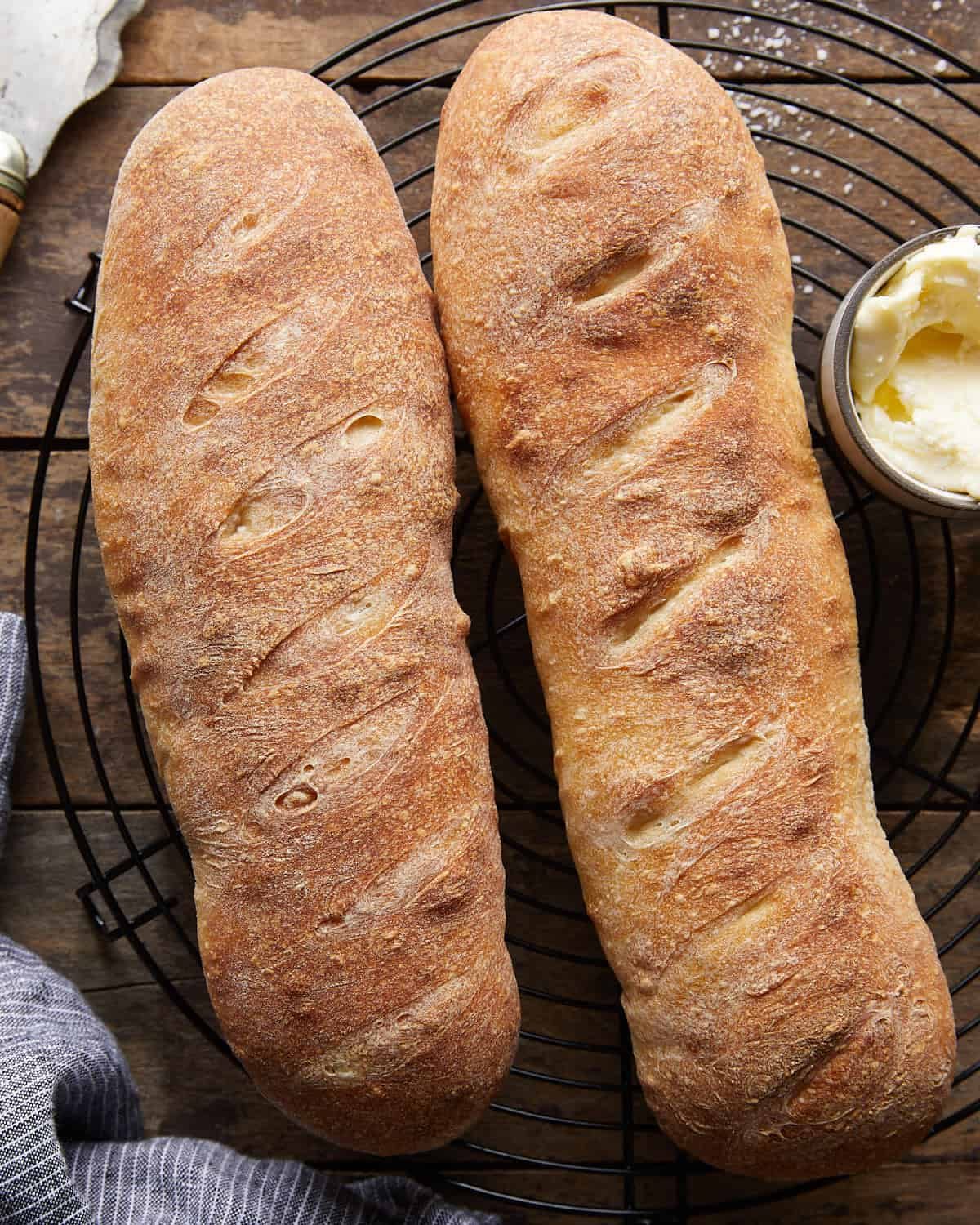 Overhead image of two loaves of French bread on wire rack with butter on the side.