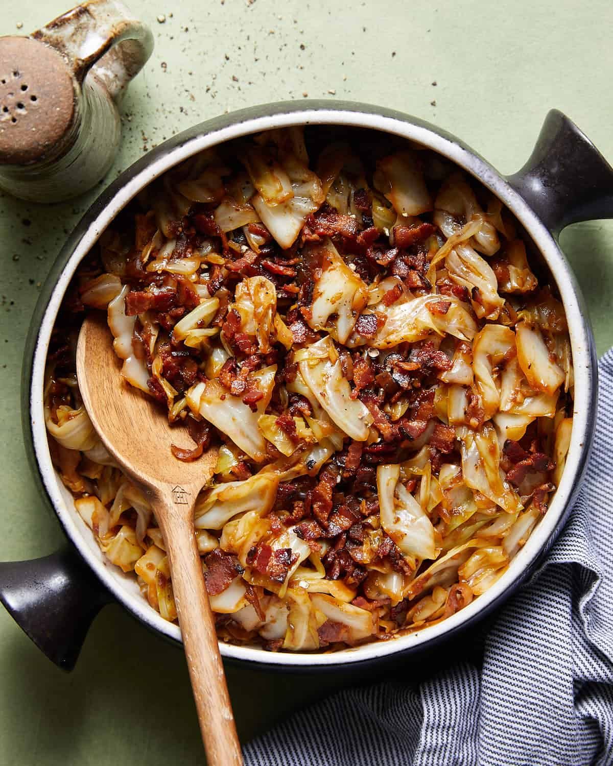 Overhead image of fried cabbage with bacon & onions in black pot.