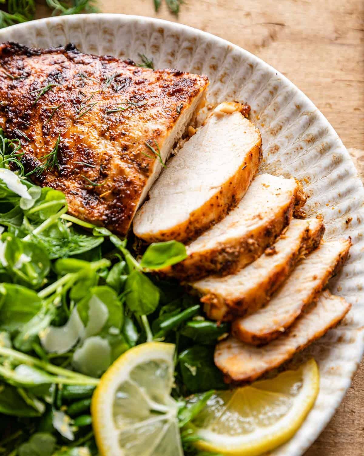 Up close image of air fryer frozen chicken breasts with side salad and lemon.