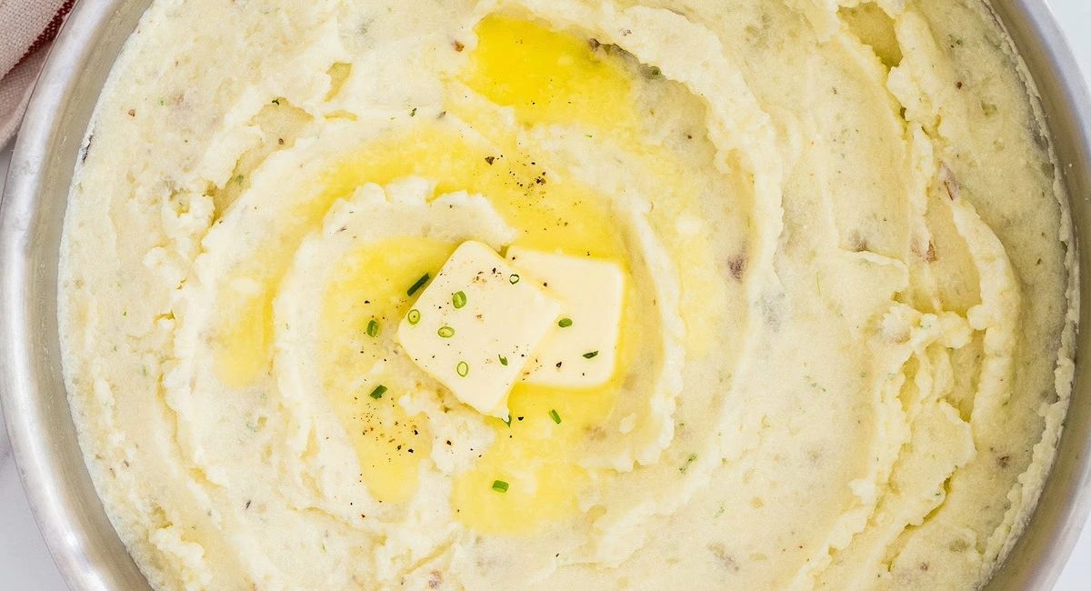 Overhead image of garlic herb mashed potatoes with butter and garnish.
