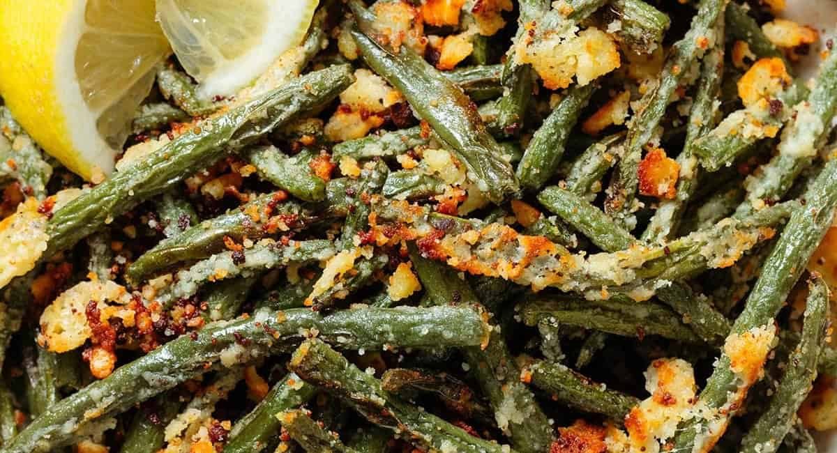 Overhead image of garlic parmesan green beans with lemon wedges.