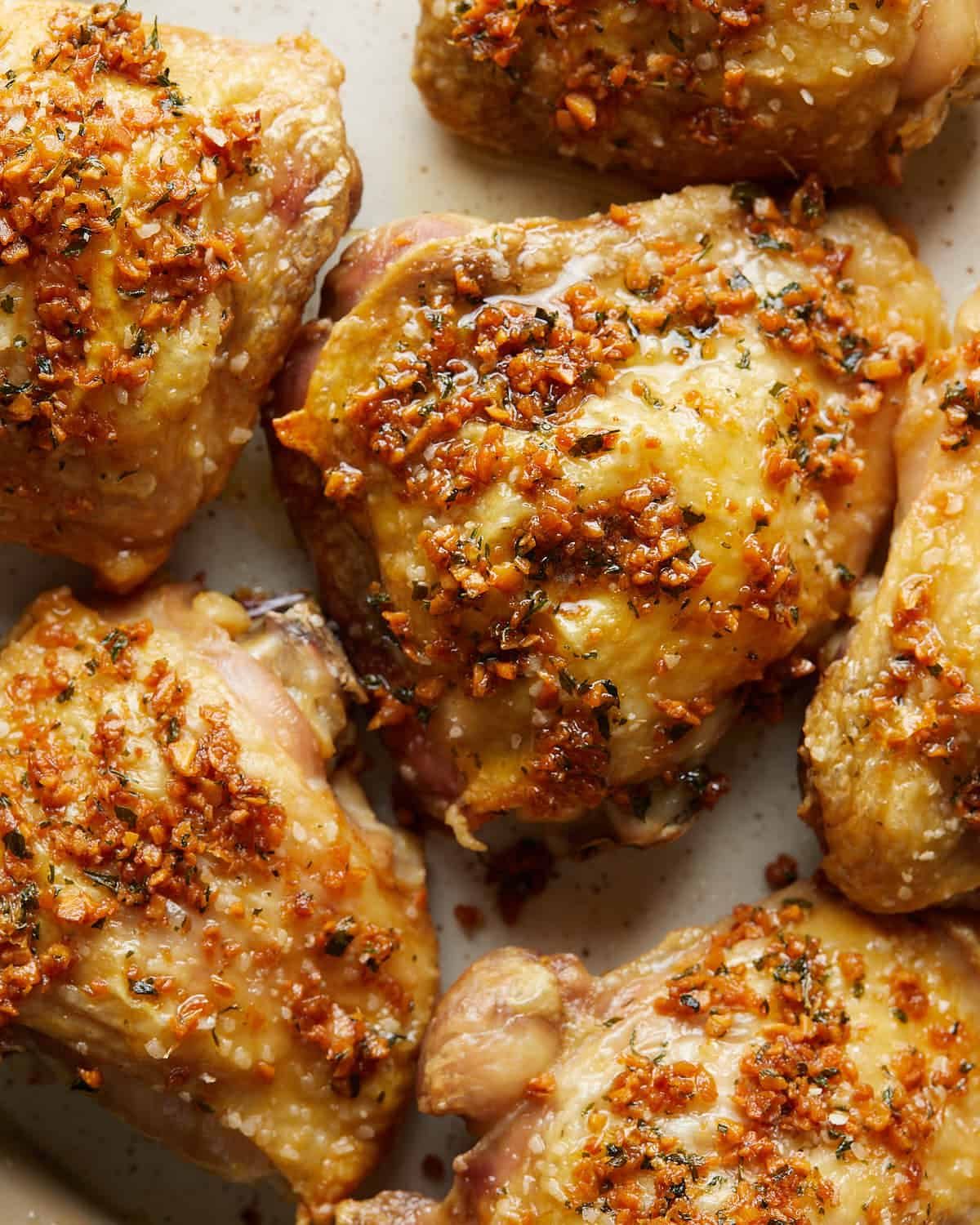 Up-close overhead photo of garlic butter chicken thighs on a plate, coated in rich garlic butter sauce and finished with fresh herbs, showcasing juicy, golden-browned chicken thighs ready to serve.
