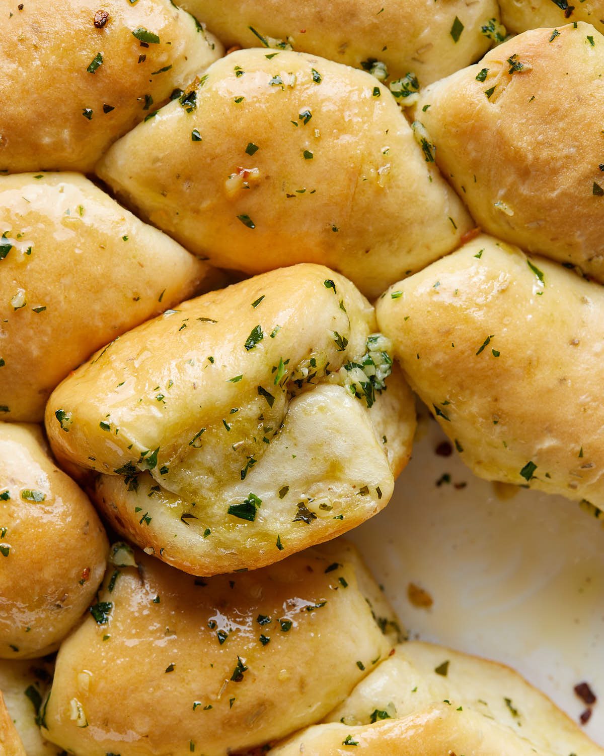 Overhead up close image of homemade garlic rolls baked in a white baking dish, featuring golden brown tops brushed with garlic butter and herbs.