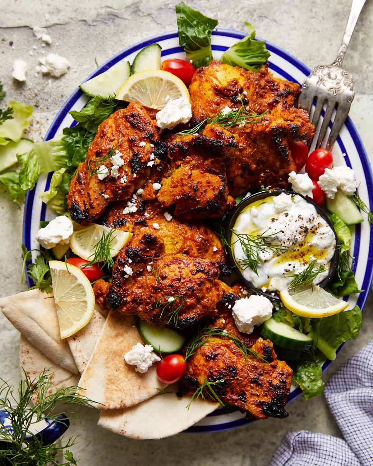 Greek yogurt marinated chicken on a platter with garnish.