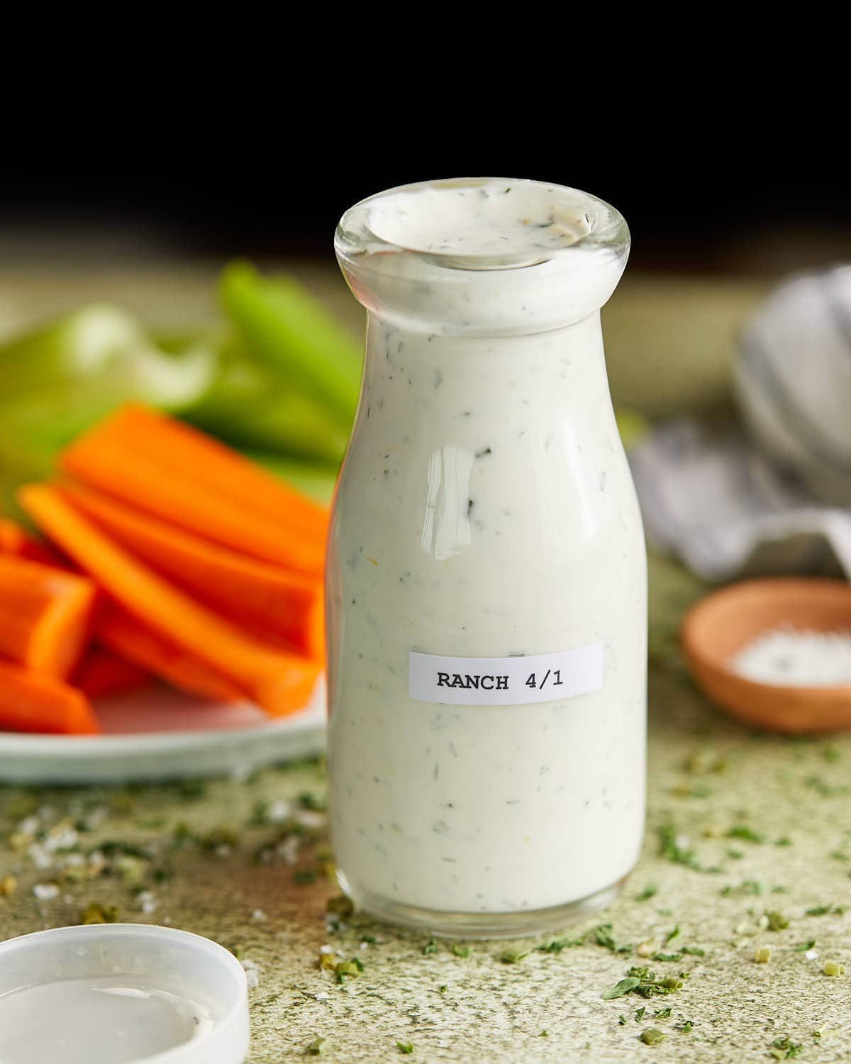 Up close image of glass jar with homemade greek yogurt ranch dressing. Carrots and celery sticks in the background.