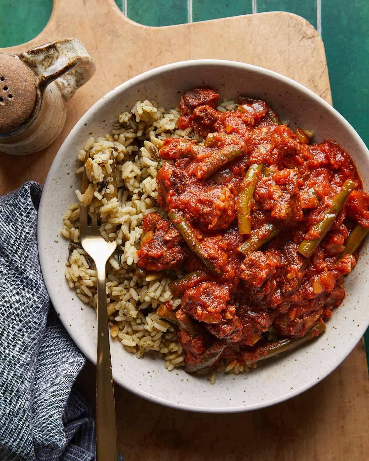 Overhead image of Lebanese green bean stew in white bowl over rice.