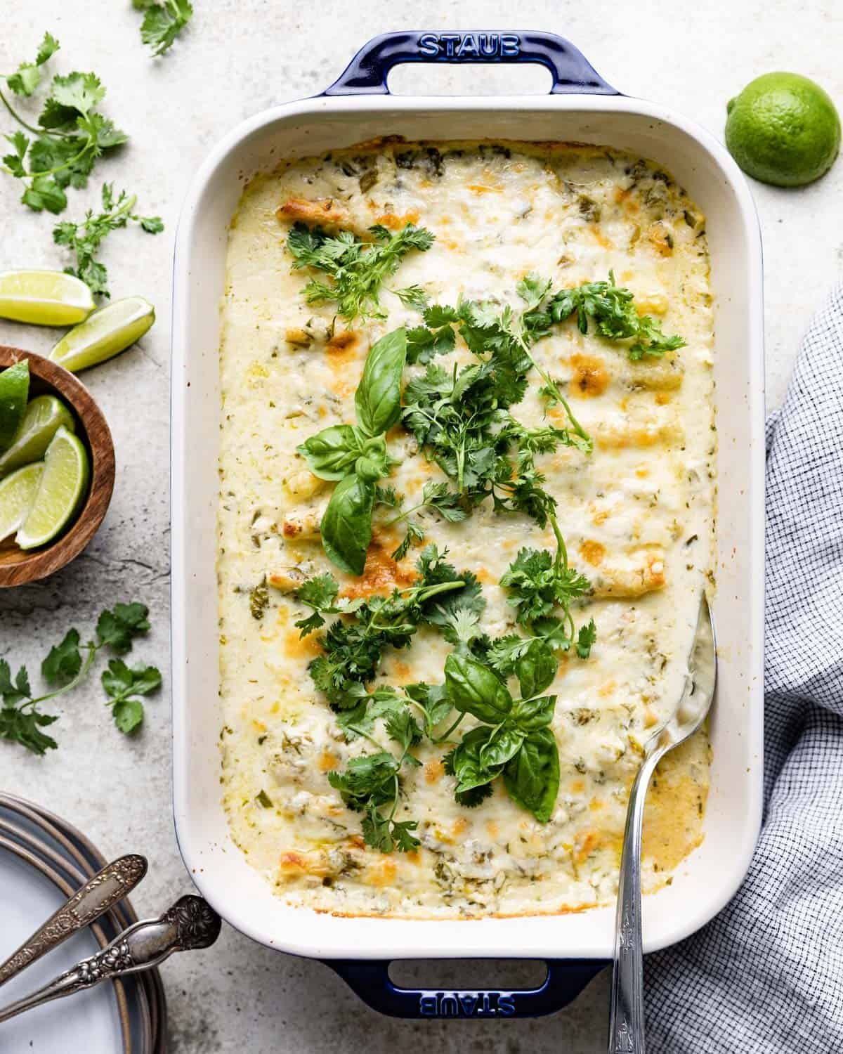 Green chili beef enchiladas with white sauce in a blue casserole dish.