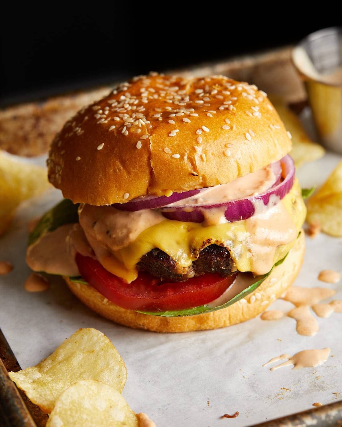 Finished cheeseburger on a sesame bun with lettuce, tomato, and red onion.