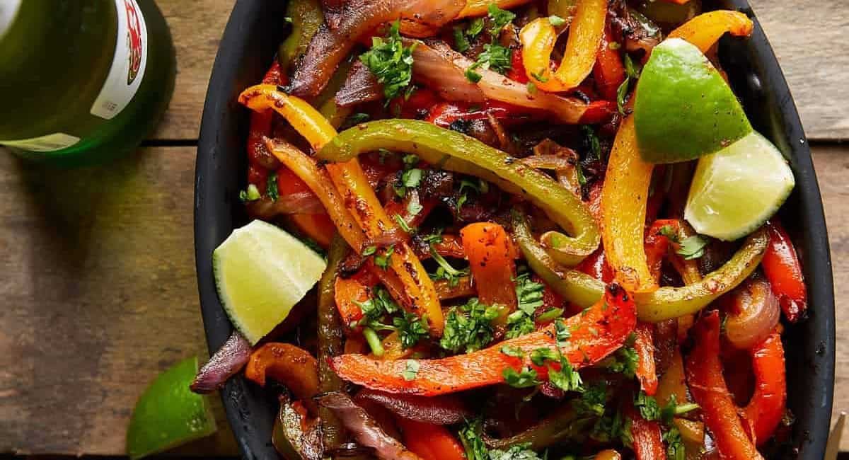 Overhead image of grilled peppers and onions with lime wedge garnish.