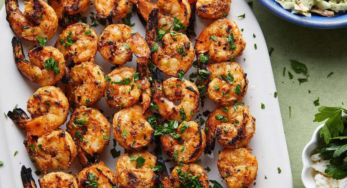 Overhead image of grilled shrimp skewers with garnish on white dish.