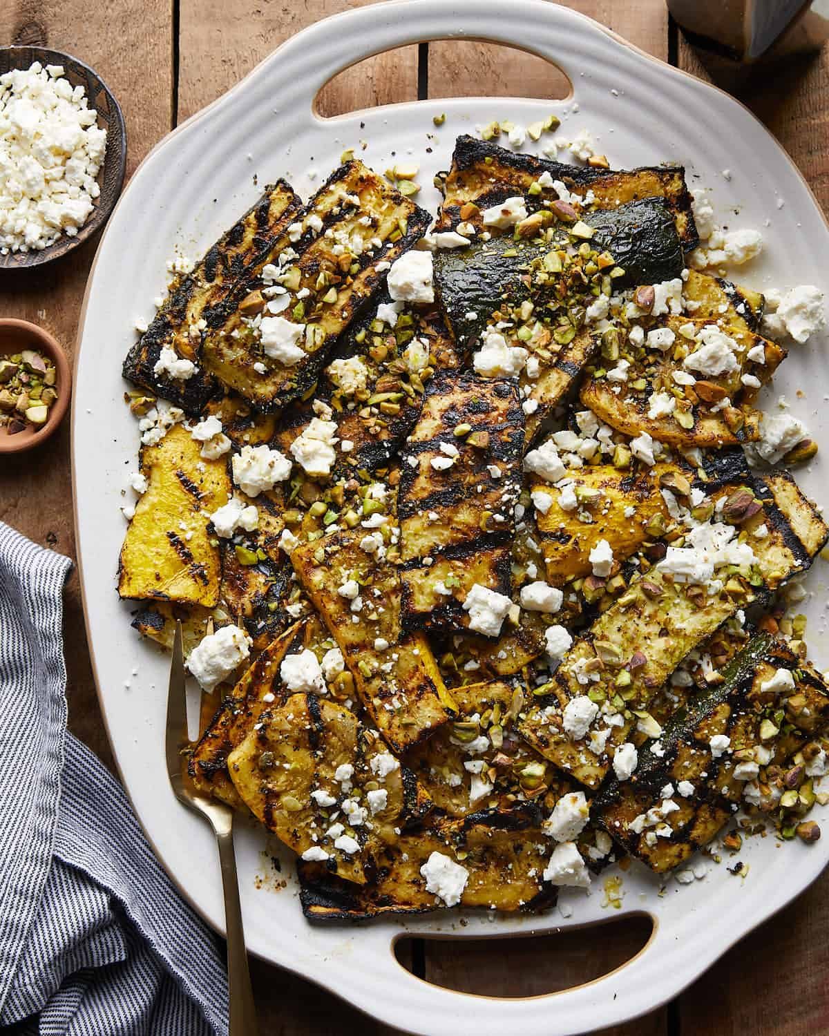 Overhead image of grilled zucchini and yellow squash with feta cheese and pistachio garnish.