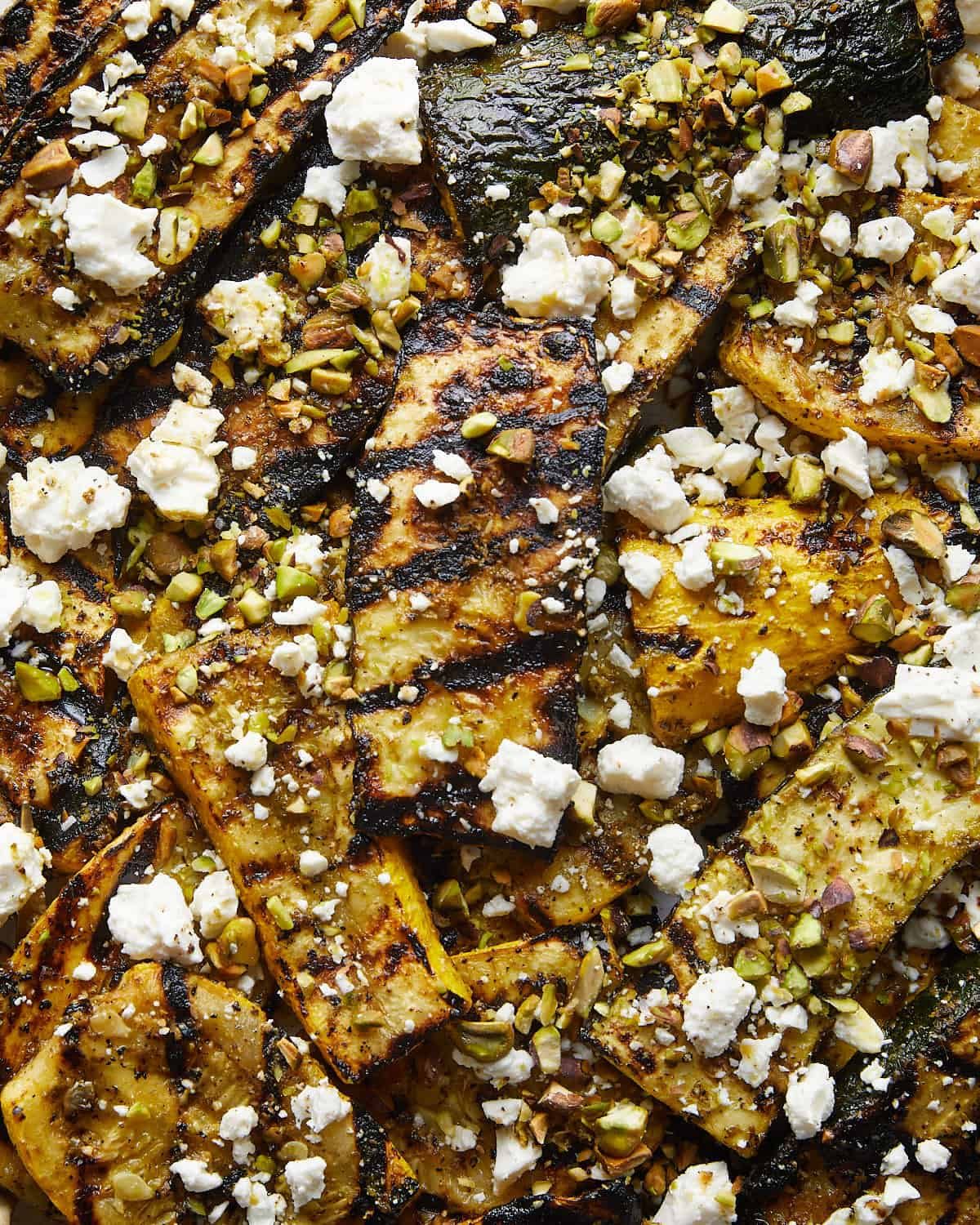 Up close image of grilled zucchini and yellow squash with feta cheese and pistachio garnish.