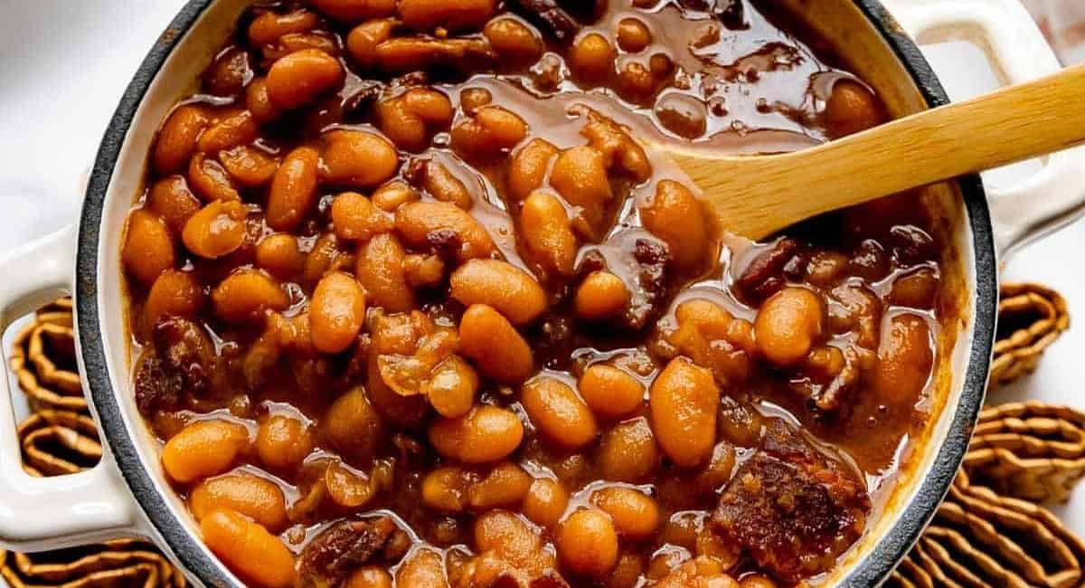 Overhead image of homemade baked beans in white dish with wooden spoon.
