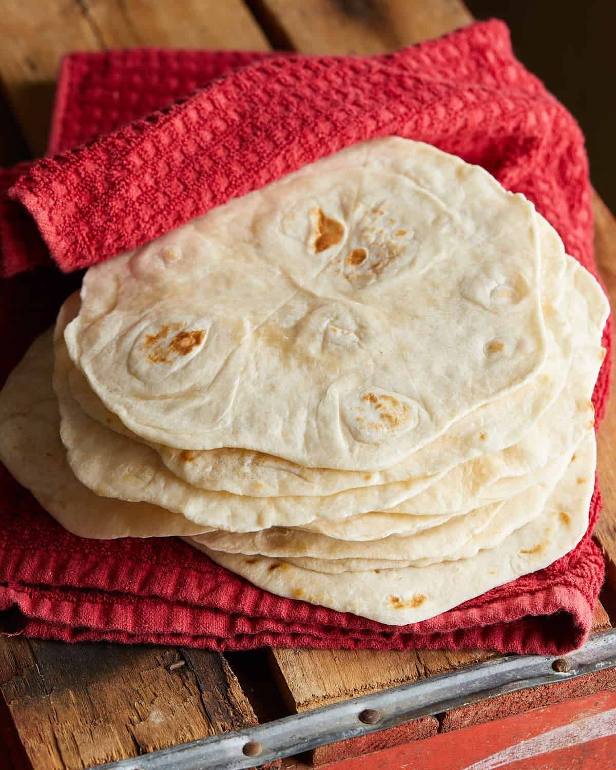 Up close image of homemade flour tortillas wrapped in red towel.