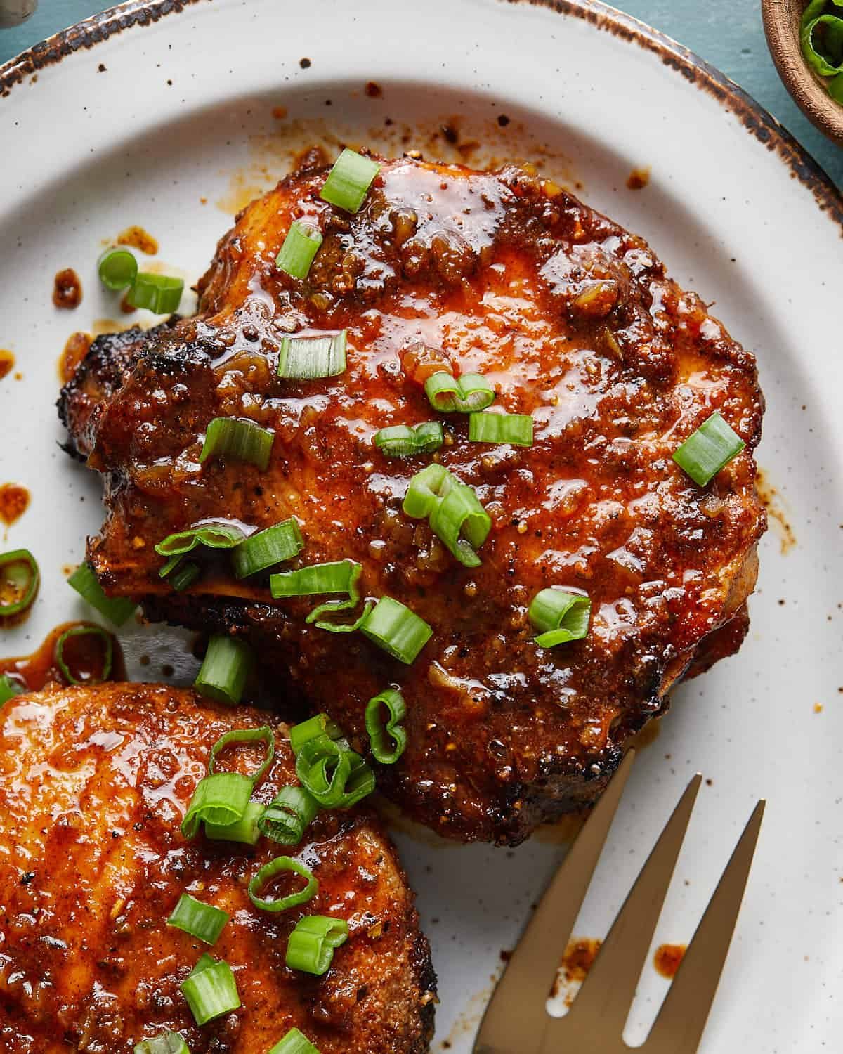 Up close photo of honey glazed pork chops with green onion garnish.