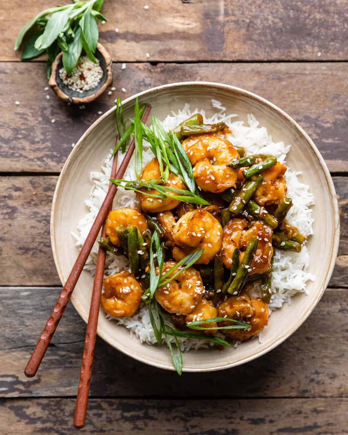 Cream colored bowl with hunan shrimp and white rice with scallions on top.