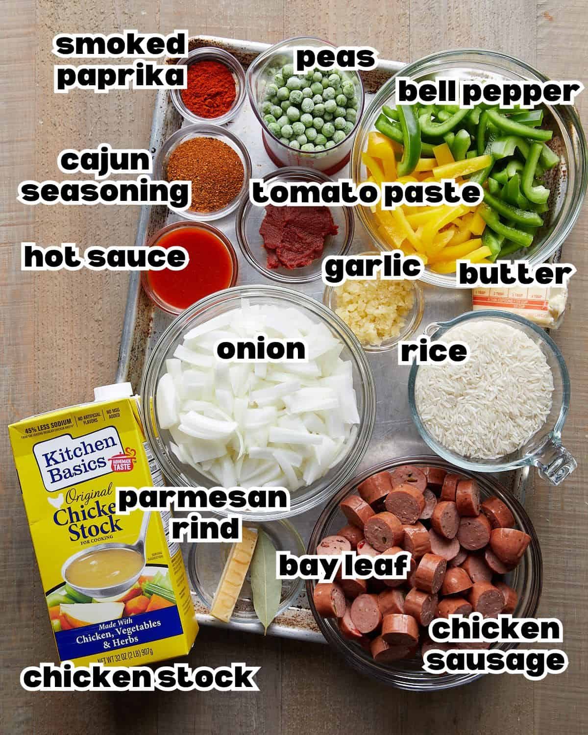 Labeled ingredients for Cajun sausage and rice: chicken sausage, rice, peppers, peas, onion, garlic, butter, chicken stock, tomato paste, Cajun seasoning, smoked paprika, hot sauce, bay leaf, and Parmesan rind.