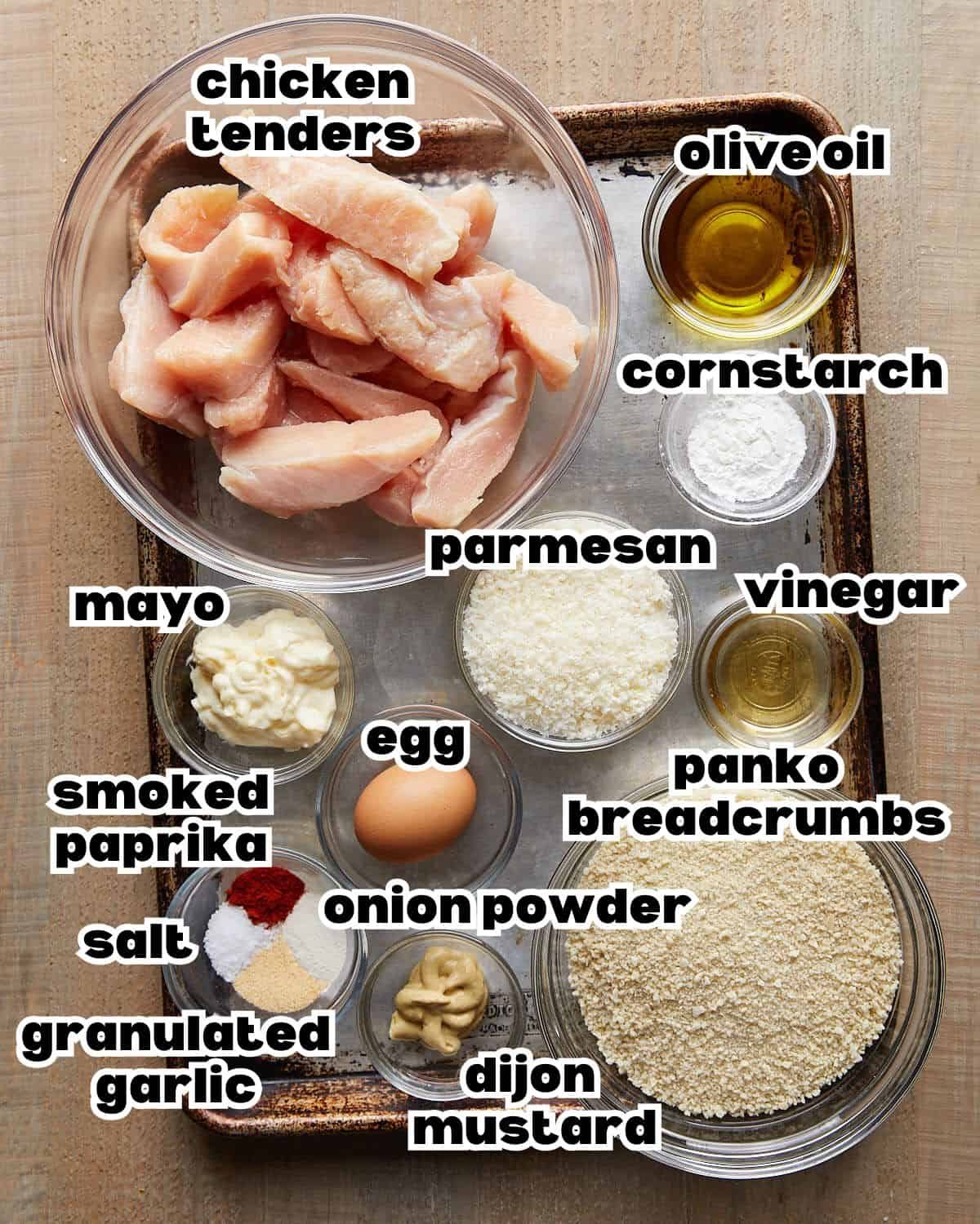Chicken tenderloins, mayonnaise, egg, apple cider vinegar, Dijon, cornstarch, olive oil, panko, Parmesan, and seasonings arranged on a sheet pan.