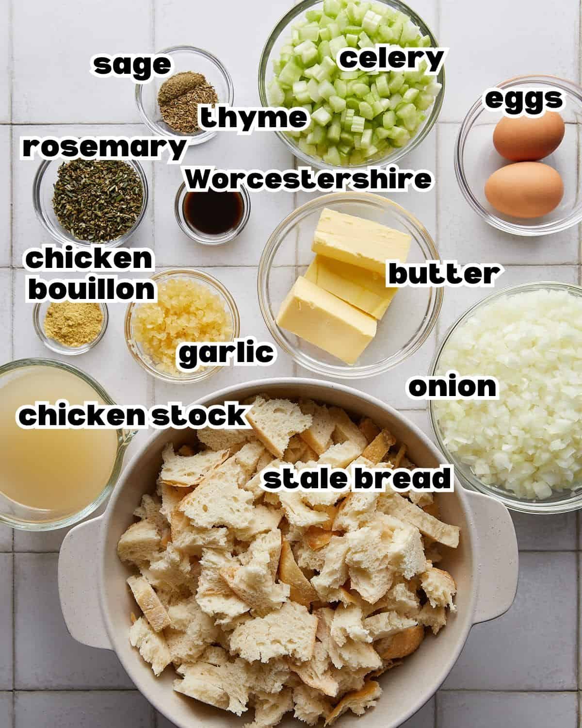 Overhead image of ingredients needed to make make ahead stuffing, including bread cubes, butter, celery, onion, herbs, broth, and seasonings arranged on a countertop.
