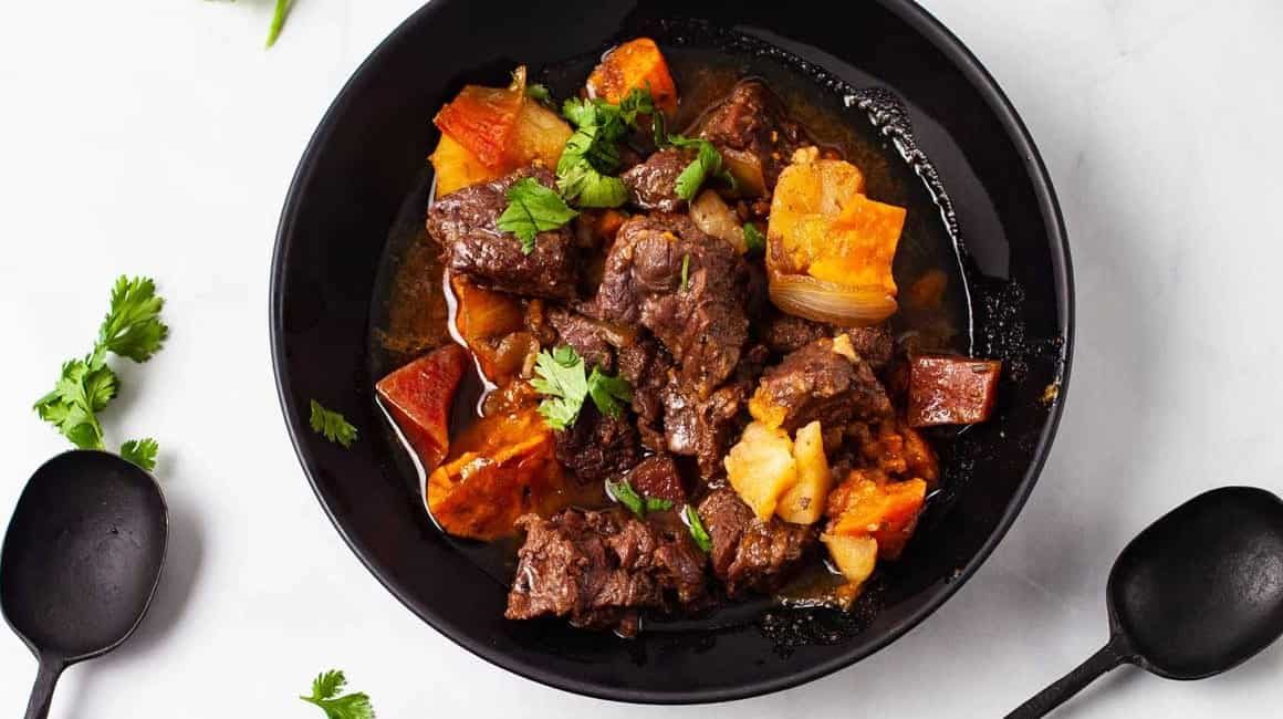Overhead image of instant pot beef stew in black dish with garnish.