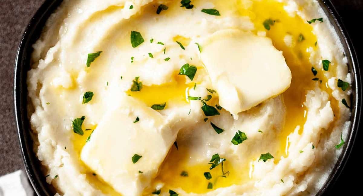 Overhead up close image of instant pot mashed potatoes with garnish in black bowl.