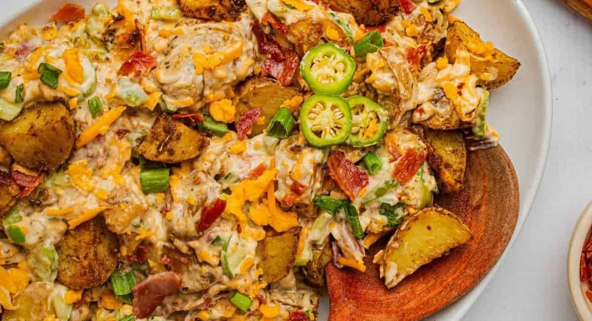 Overhead image of jalapeno popper potato salad on white dish with wooden spoon.