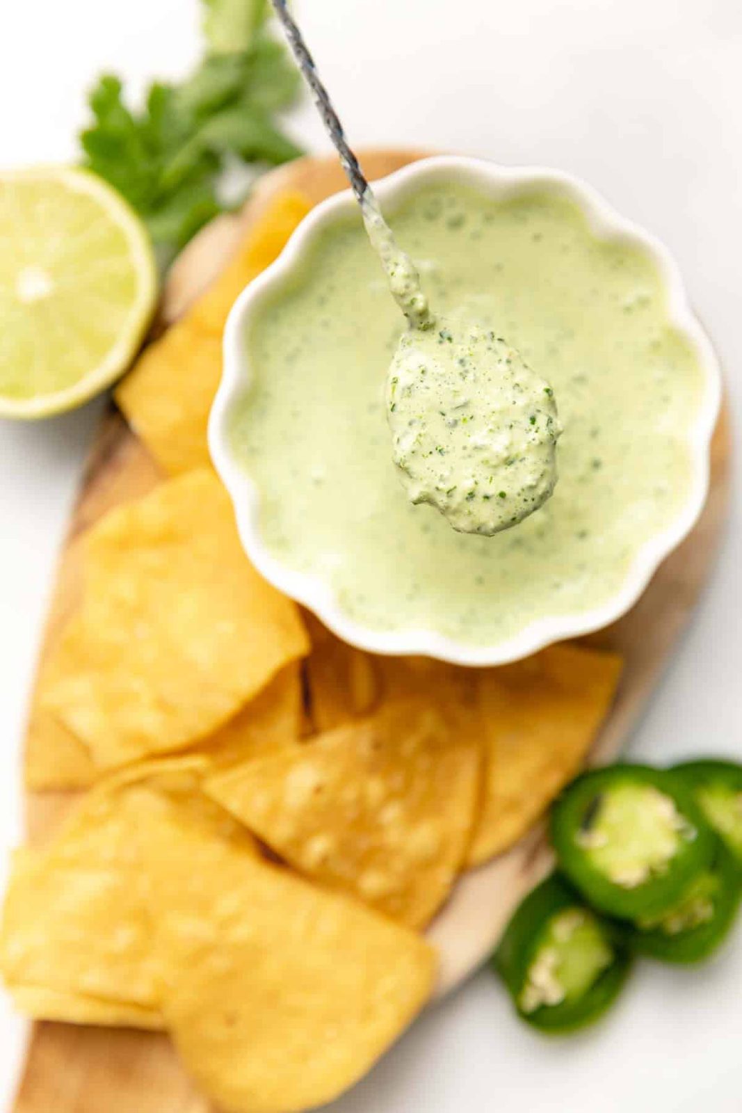 A spoonful of jalapeño lime crema above a bowl served with tortilla chips.