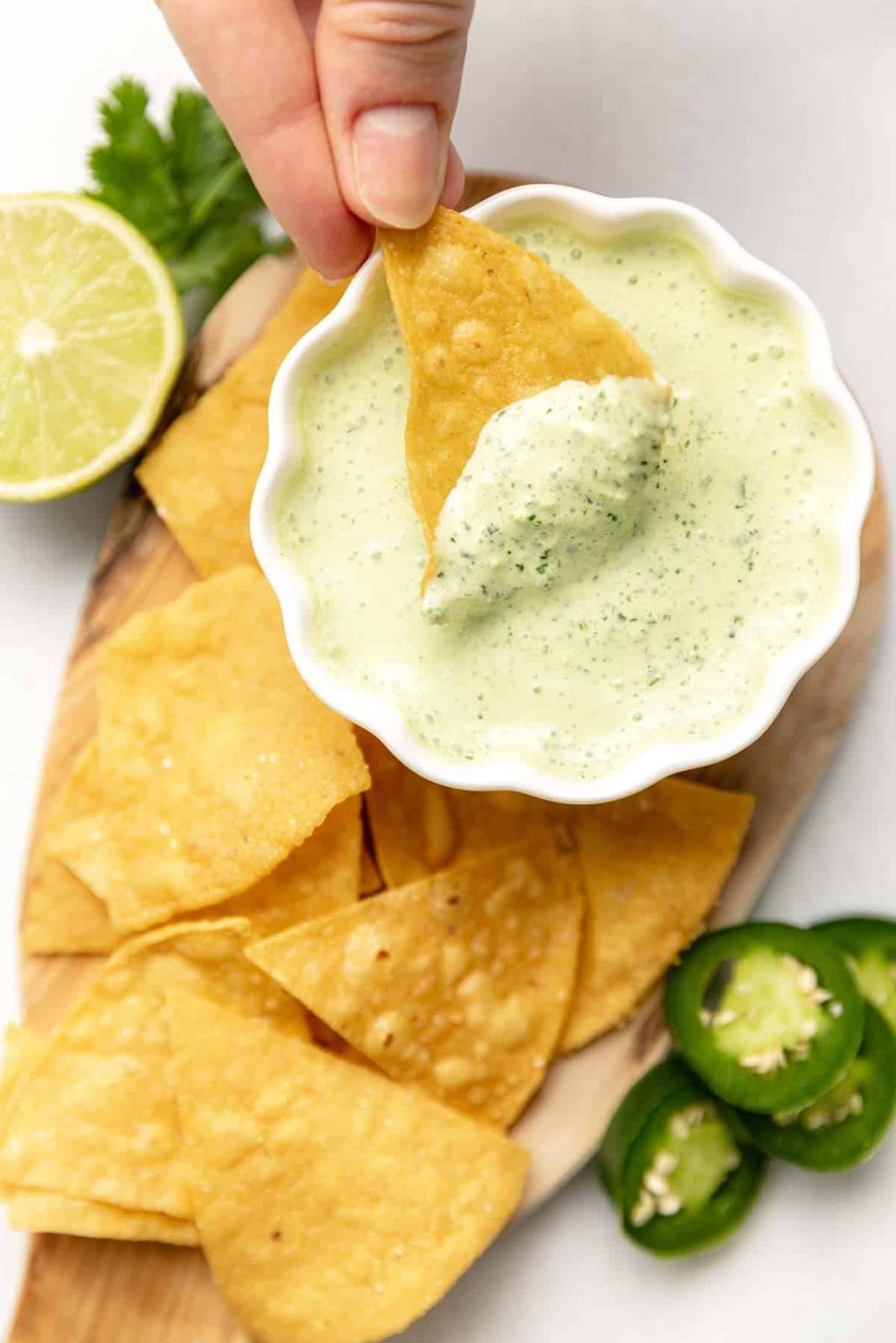 A tortilla chip dipped into a bowl of jalapeño lime crema.