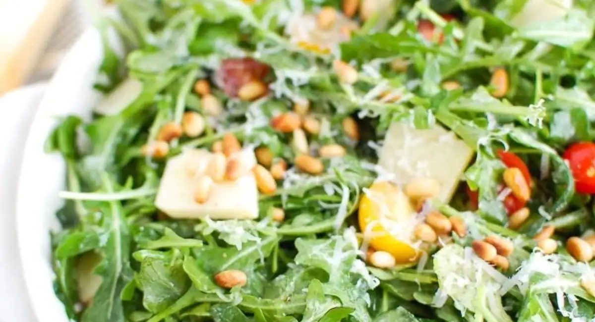 Up close overhead image of lemon arugula salad with parmesan cheese in white dish.