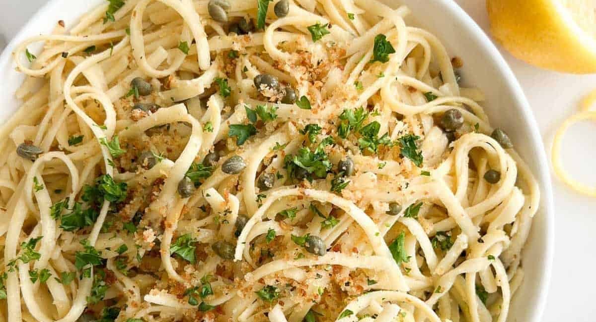 Overhead image of lemon caper pasta with garnish in white bowl.