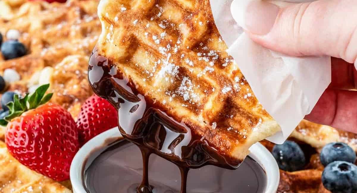 Up close image of liege waffles being dipped into chocolate sauce.