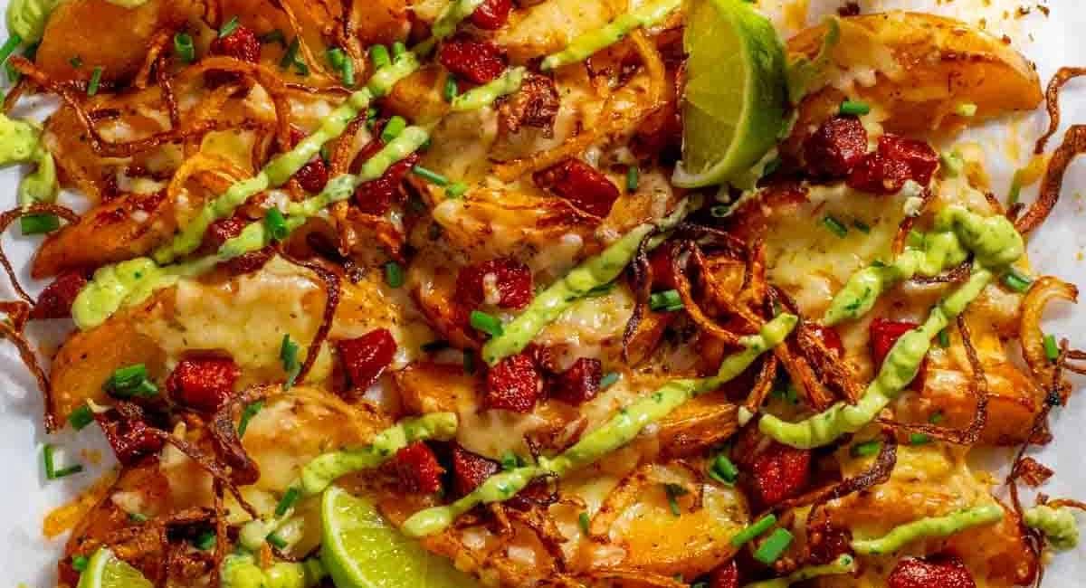 Overhead image of loaded potato wedges with chorizo and avocado sauce.