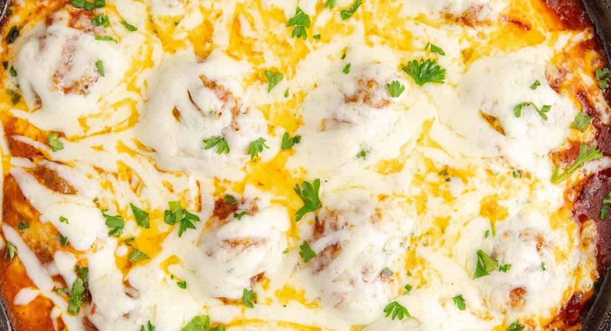 Overhead up close image of meatball parmigiana with garnish.