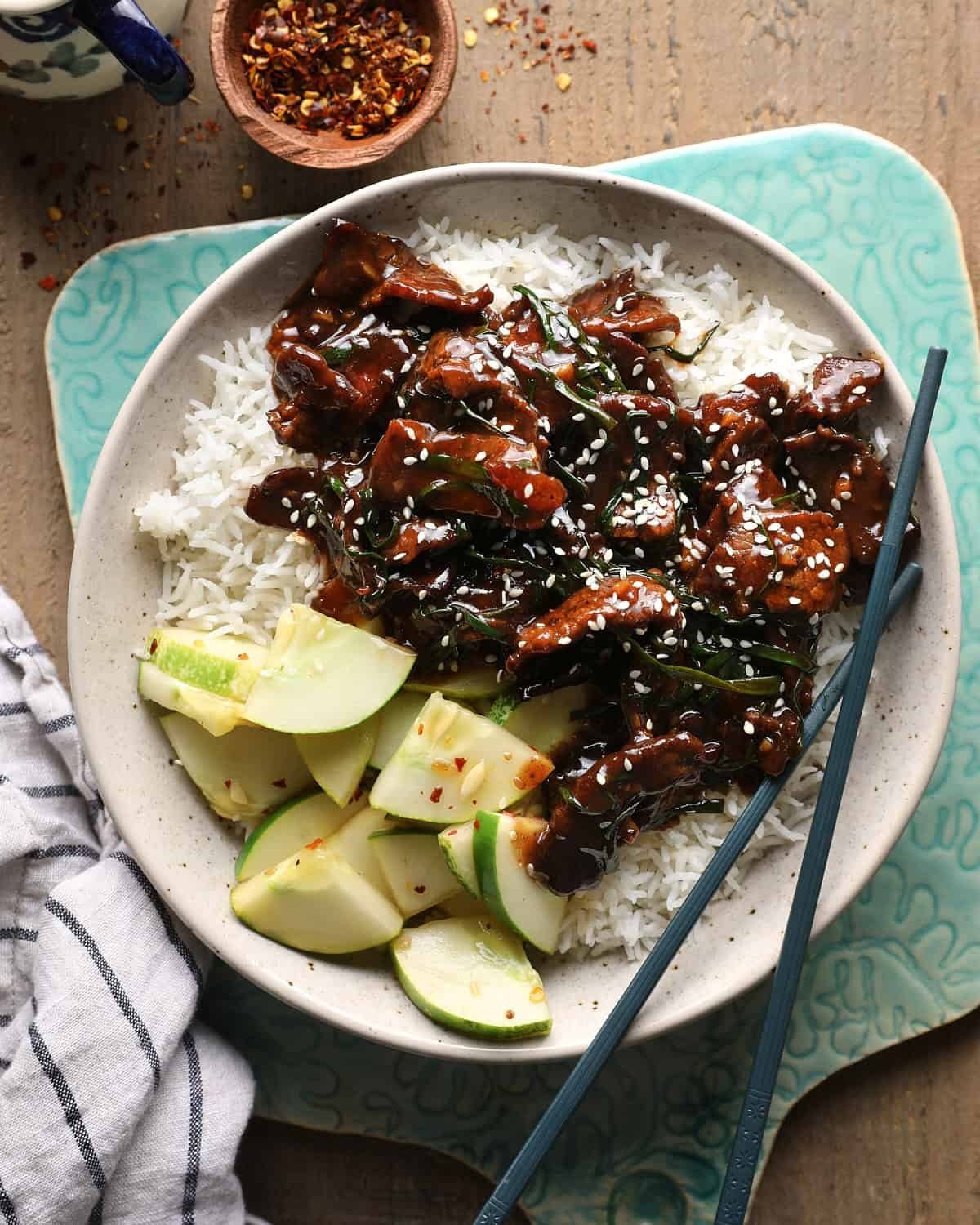 Mongolian beef served over rice with cucumber slices and green onions.