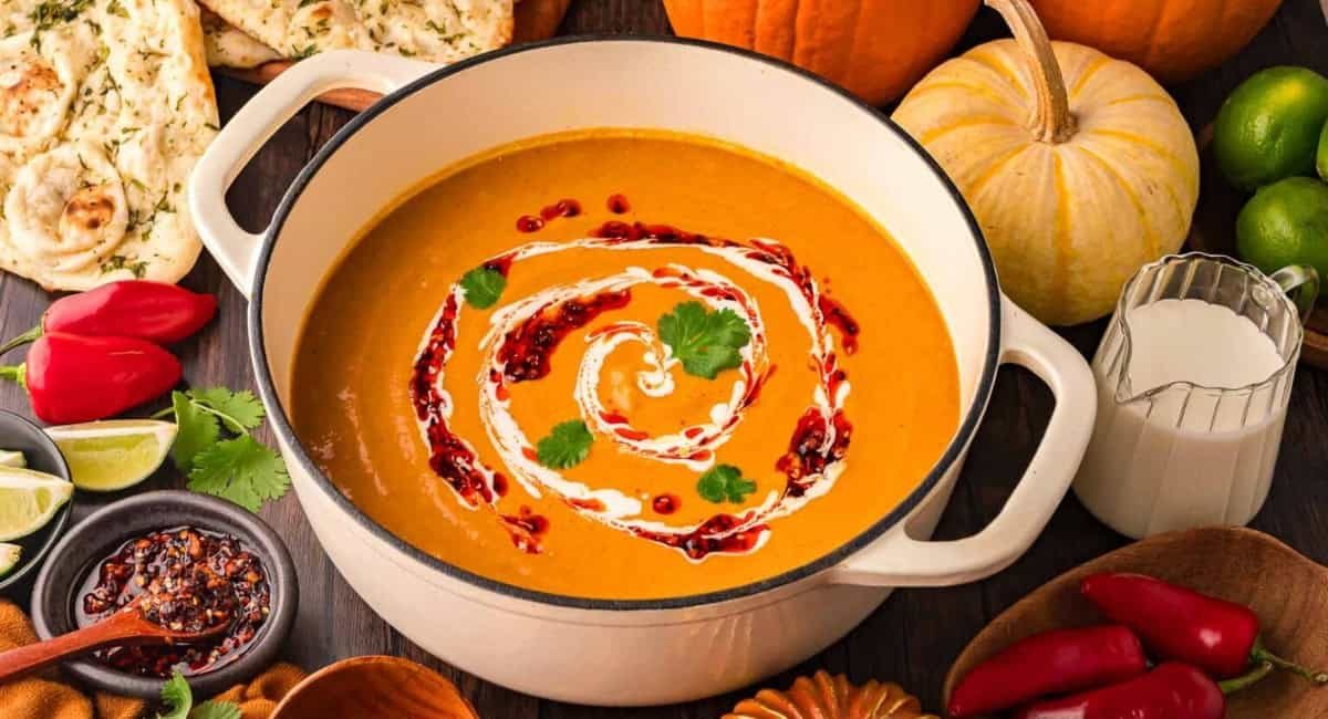 Overhead image of pumpkin coconut curry soup with garnish in white pot.