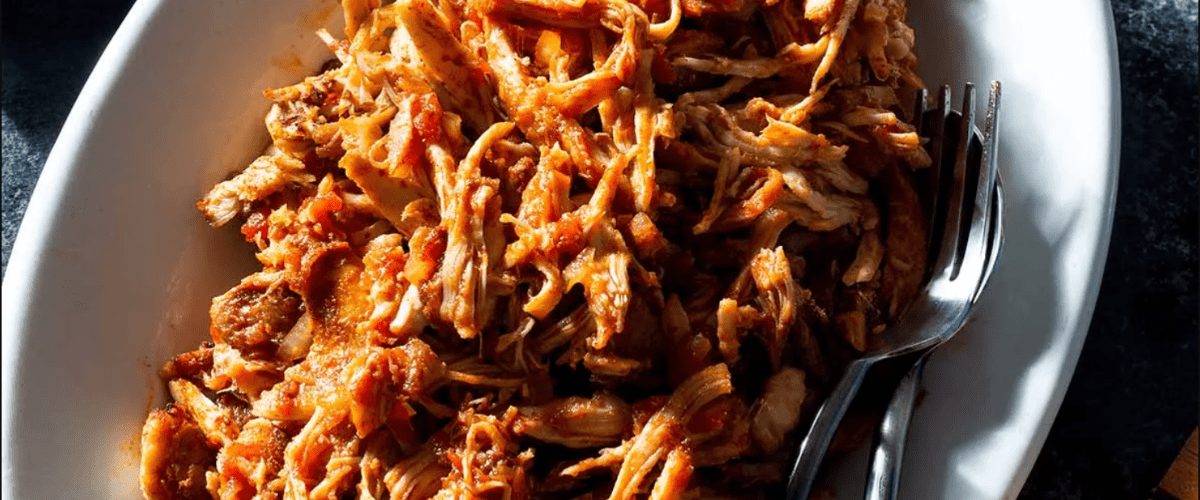 Oven pulled chicken thighs in white dish with fork.