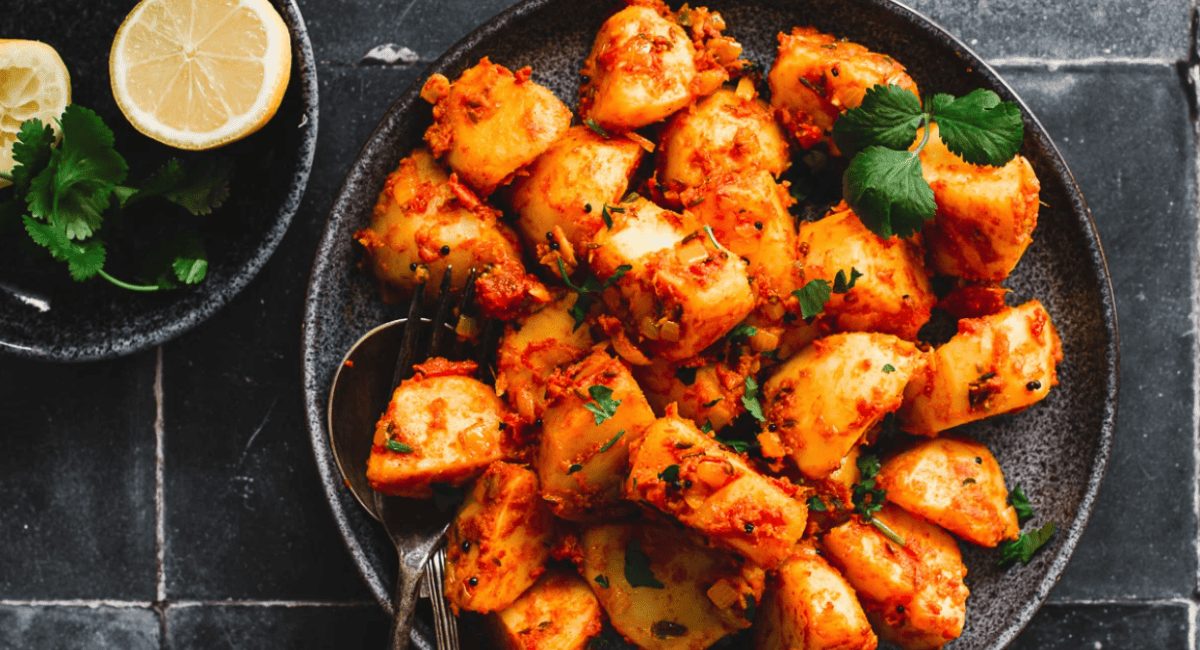 Overhead image of bombay potatoes with garnish on black dish.