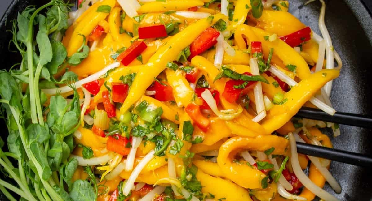 Overhead image of simple thai mango salad in black dish with chopsticks.