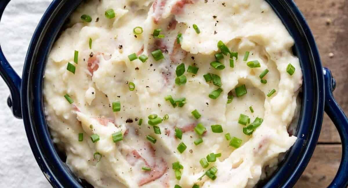 A photo of red skin mashed potatoes with garnish.