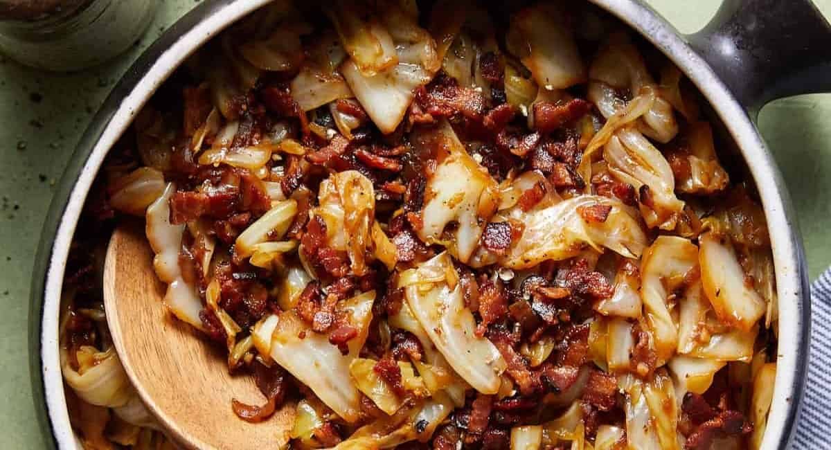 Overhead image of fried cabbage with bacon and onions in black dish.