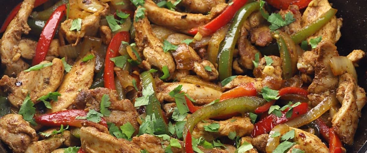 Skillet chicken fajitas with bell pepper veggies and garnish.