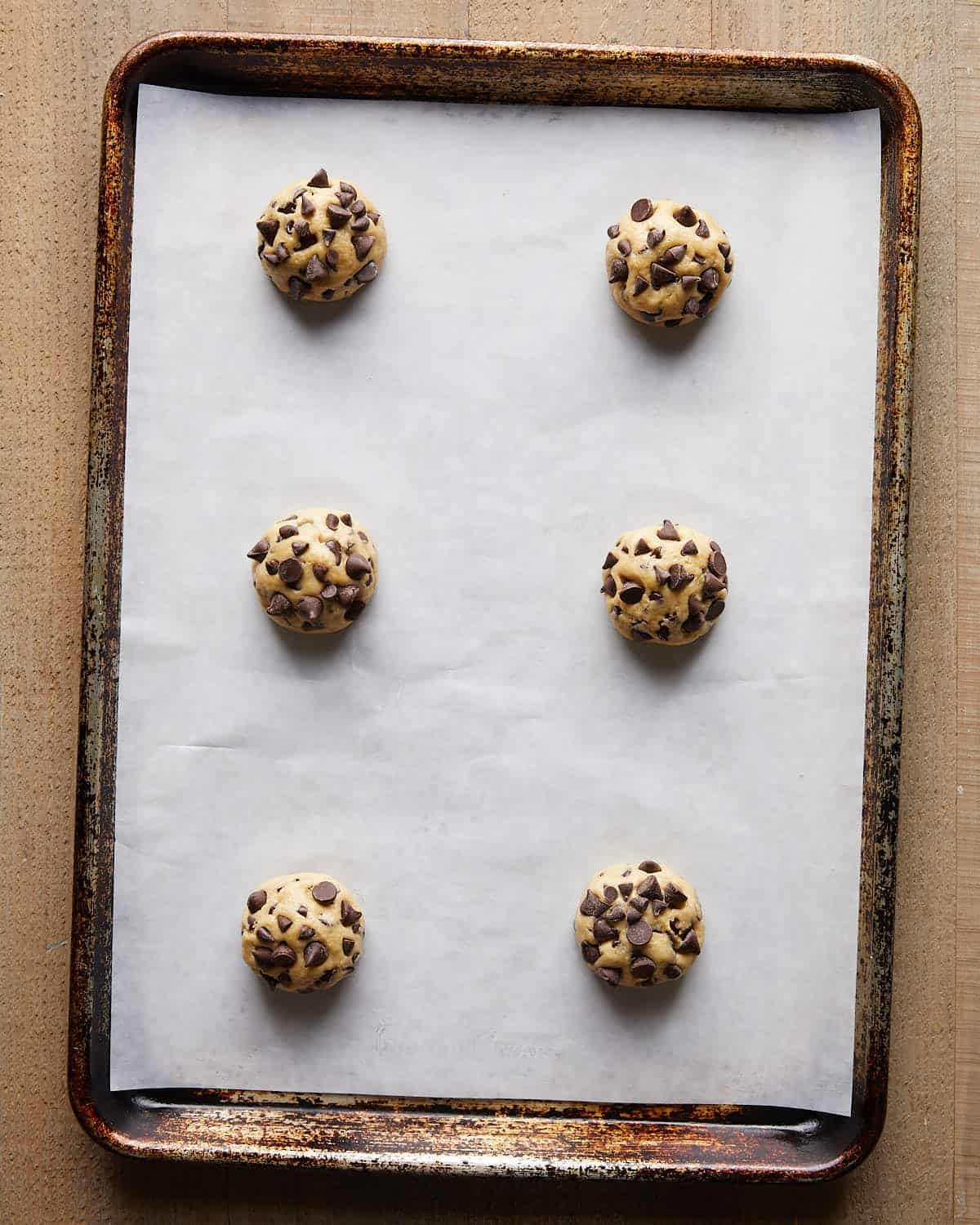 Overhead image of portioned no chill chocolate chip cookie dough placed on a parchment-lined baking sheet, ready to bake for soft, chewy cookies.