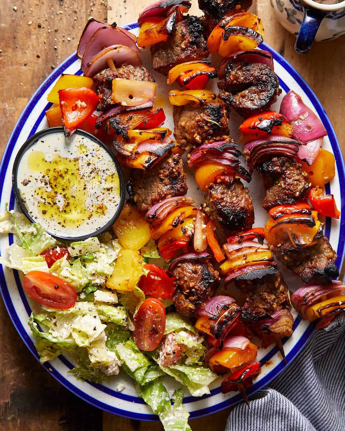 Overhead image of beef kabobs on white and blue dish.