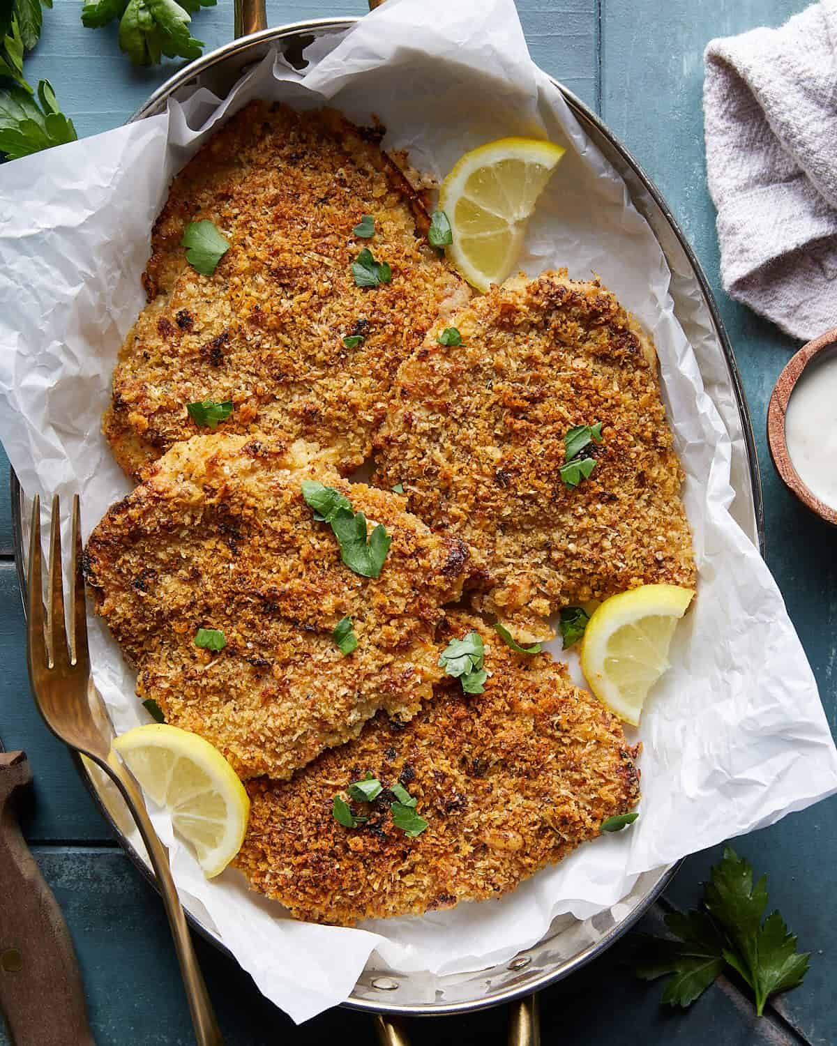 Baked panko chicken breasts with a golden Parmesan-panko topping, parsley, and lemon wedges.