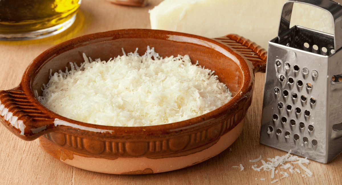 Up close image of Pecorino Romano in a brown dish with cheese grater next to it.