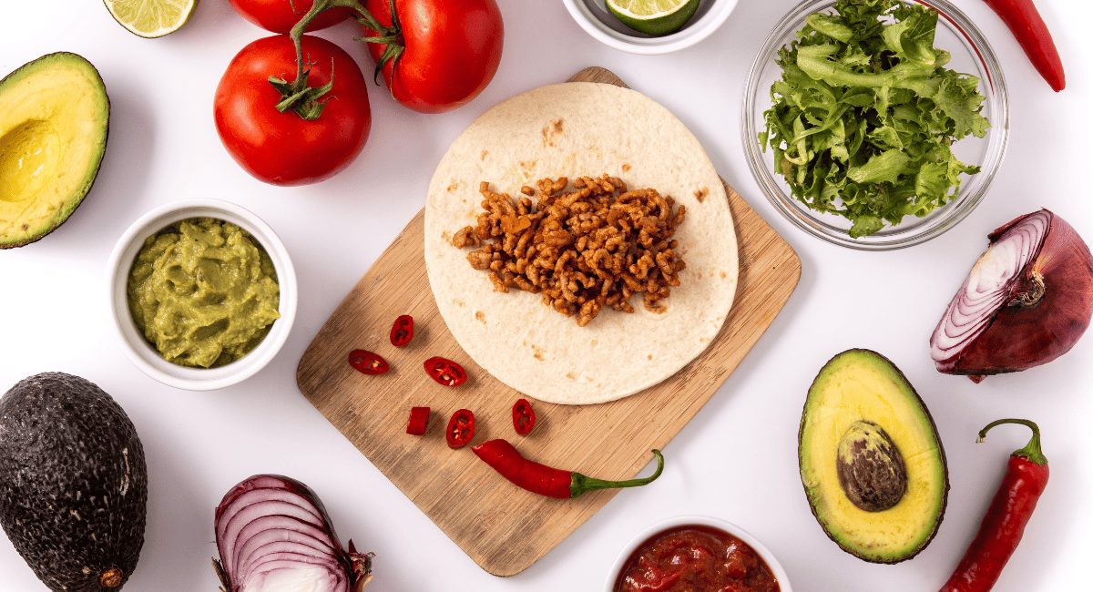 Overhead image of plain ground beef taco with veggies surrounding it.